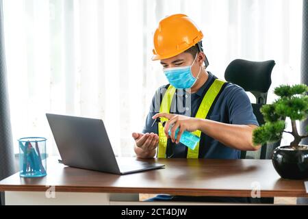 quarantine, happy asian engineer wearing face protective medical mask for protection from virus disease with laptop computer using hand sanitizer in c Stock Photo