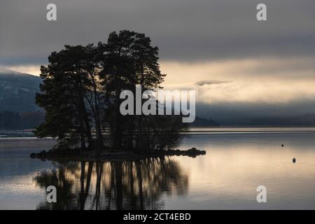 Lone trees on an island reflecting in Loch Tay Lake at sunset with dramatic sunset sky reflections, Kenmore, Perthshire, Highlands of Scotland, United Kingdom, Europe Stock Photo