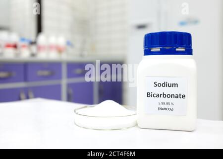 Selective focus of a bottle of sodium bicarbonate chemical compound or baking soda beside a petri dish with solid crystalline powder substance Stock Photo