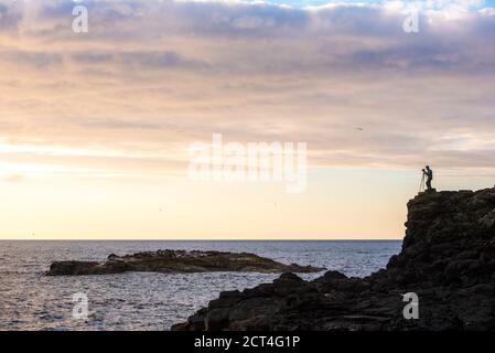 Landscape Photographer silhouette on the dramatic coast, photographing the ocean, County Antrim in Northern Ireland, background with copy space Stock Photo