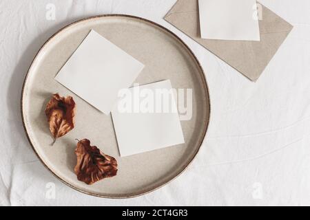 Autumn composition. Blank memo cards mockups, craft envelope and dry beech leaves on white linen table cloth background. Fall and Thanksgiving concept Stock Photo