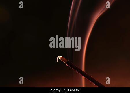 Closeup of a burning incense against a dark blurry background Stock Photo
