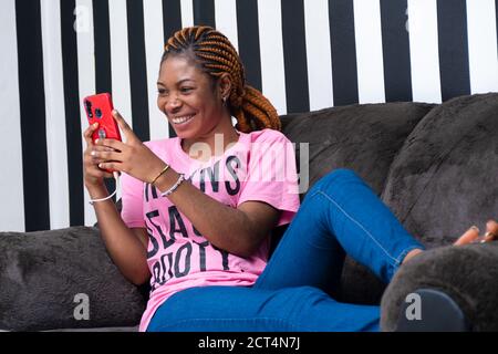 young african lady sitting on a couch using her phone while it is charging Stock Photo