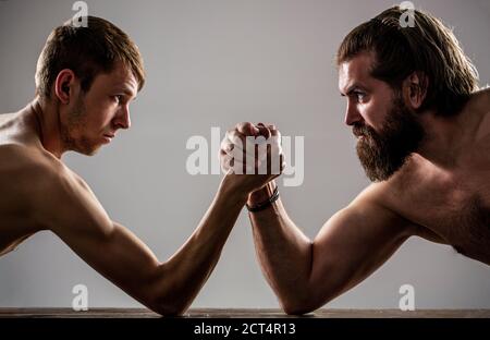 Arms wrestling thin hand, big strong arm in studio. Two man's hands clasped arm wrestling, strong and weak, unequal match. Heavily muscled bearded man