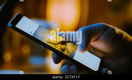 Close-up Macro: Person Holding and Using Smartphone, Browsing through Pictures on Social Network Wall. Finger Scrolling Social Media App Feed: Travel Stock Photo