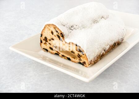 Closeup of half a Marzipan Christstollen, German Stollen, Weihnachtsstollen, on a white plate and grey textured background with copy space. Low angle Stock Photo