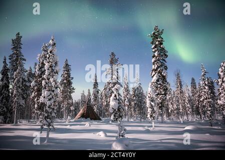 Northern Lights (aurora borealis) above a tent teepee kota in the forest in winter in Finnish Lapland, inside Arctic Circle in Finland Stock Photo