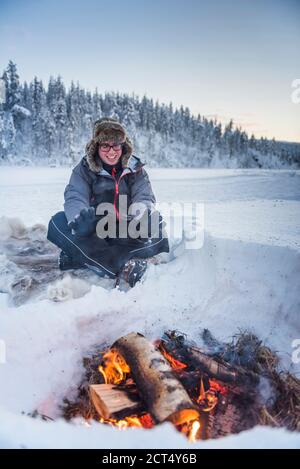 Person sat at a camp fire warming himself on a freezing cold day in winter in the Arctic Circle in Lapland, Finland