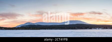 Cold weather and snow covered icy winter landscape with dramatic sunset sky and clouds over a frozen lake inside the Arctic Circle in Lapland in Finland Stock Photo