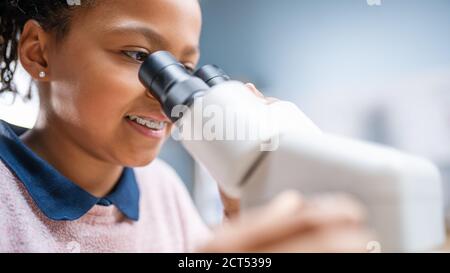 Portrait of Smart Little Schoolgirl Looking Under the Microscope. In Elementary School Classroom Cute Girl Uses Microscope. STEM science, technology Stock Photo