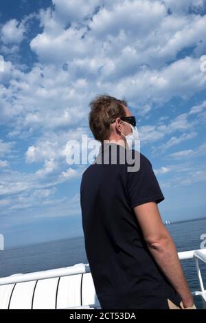 a middle aged french male passenger wearing a facial mask against Covid stands looking out to sea on a ferry in Brittany during summer holidays France Stock Photo