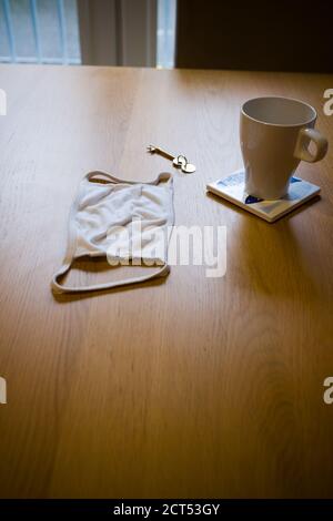 A reusable white cotton lies next to a door key and a mug on a place mat on a wooden kitchen table in a morning domestic environment Stock Photo