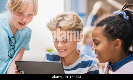 Elementary School Computer Science Class: Two Girls and Boy Use Digital Tablet Computer with Augmented Reality Software, They re Excited, Full of Stock Photo