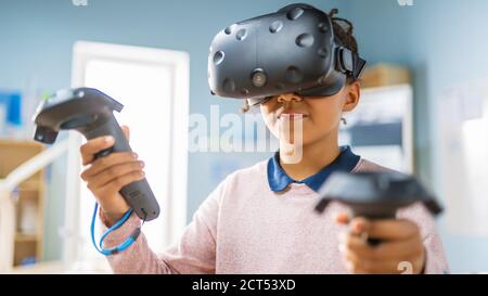 Elementary School Computer Science Class: Cute Girl Wearing Augmented Reality Headset and Using Controllers Learns Lessons in Virtual Reality Excited Stock Photo