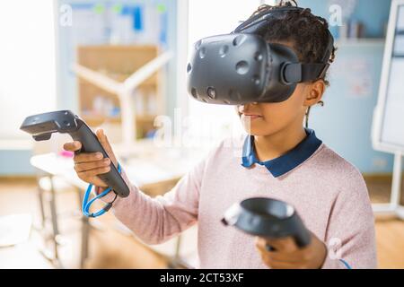 Elementary School Computer Science Class: Cute Girl Wearing Augmented Reality Headset and Using Controllers Learns Lessons in Virtual Reality Excited Stock Photo