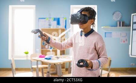 Elementary School Computer Science Class: Cute Girl Wearing Augmented Reality Headset and Using Controllers Learns Lessons in Virtual Reality Excited Stock Photo