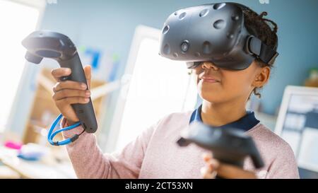 Elementary School Computer Science Class: Cute Girl Wearing Augmented Reality Headset and Using Controllers Learns Lessons in Virtual Reality Excited Stock Photo