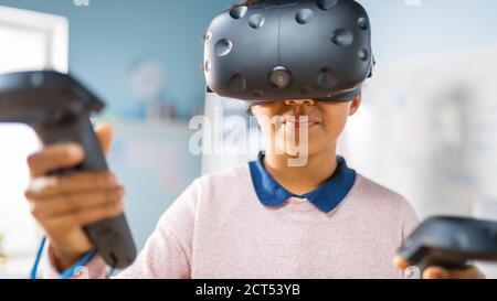 Elementary School Computer Science Class: Cute Girl Wearing Augmented Reality Headset and Using Controllers Learns Lessons in Virtual Reality Excited Stock Photo