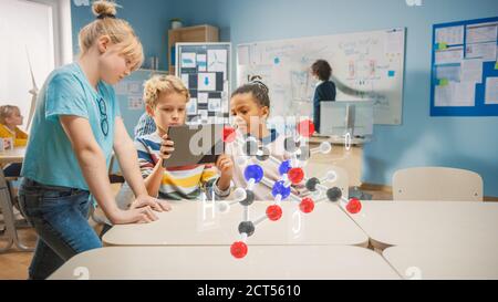 Three Diverse School Children in Chemistry Science Class Use Digital Tablet Computer with Augmented Reality Application, Looking at Educational 3D Stock Photo