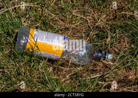An empty plastic drink bottle with text on a yellow and white label, lying on some scrubby grass having been thrown away as litter Stock Photo