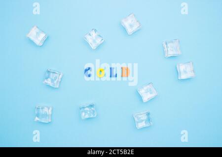 The word COLD on a blue background of wooden multicolored letters, ice cubes around the word. Stock Photo