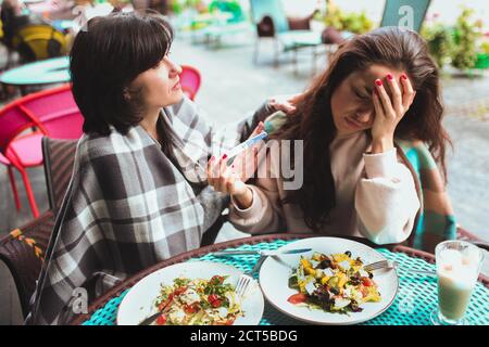 Mature mother and her young daughter sit together in cafe or restaurant. Upset worry girl showing positive pregnancy test to her mom. Mature woman try Stock Photo