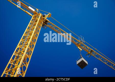 Bottom up view of a yellow crane lifting up a weight in a building site on a flat blue sky background Stock Photo