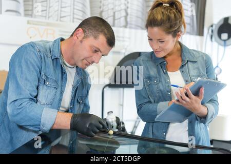 two glaziers replace windshield of a car in workshop Stock Photo