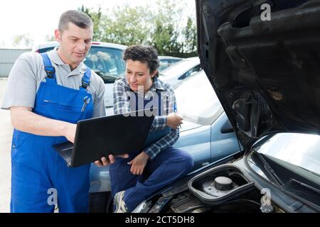 female and male mechanic using laptop for examining car engine Stock Photo