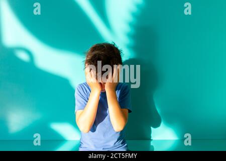 Portrait of a sad or frustrated brunette boy in a blue shirt. thumbs up. turquoise background with shadow. Education. Looking and smiling at the camera Stock Photo
