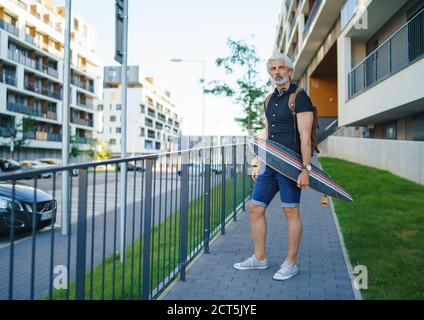 Portrait of mature man with skateboard outdoors in city, going back to work. Stock Photo