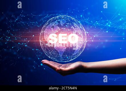 Hand Holding Holographic World Globe With Word Seo, Blue Background Stock Photo