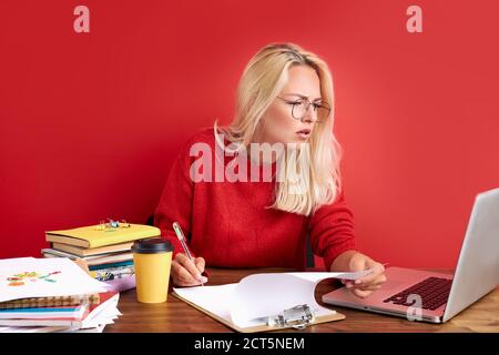 woman is concentrated on work on laptop, she is looking at screen and think, write information on paper Stock Photo
