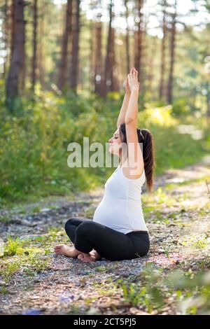 Portrait of happy pregnant woman outdoors in nature, doing yoga exercise. Stock Photo
