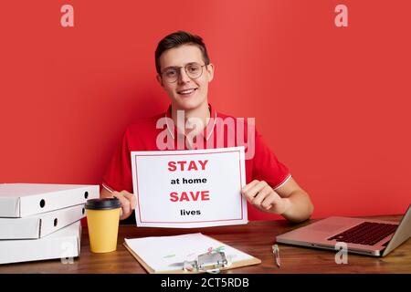 open-minded caucasian male ask people stay home during quarantine, work with laptop, at freelance, isolated red background Stock Photo