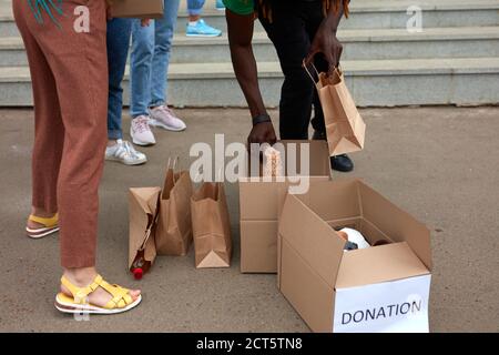 group of diverse people sort through donated food items while volunteering in community, they use cardboard boxes for collecting donation Stock Photo