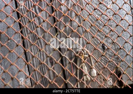 Old metal mesh covered in rust and an old wooden wall at the back, close-up, selective focus Stock Photo