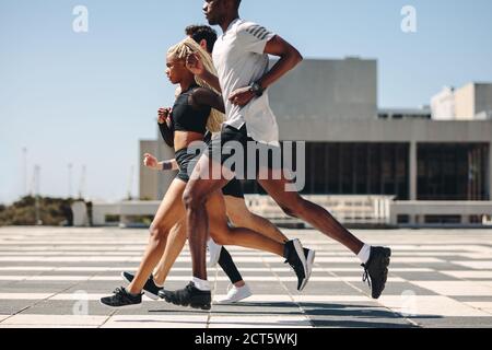 Group of men and women running together in the city. Multiracial street runners exercising in the city. Stock Photo