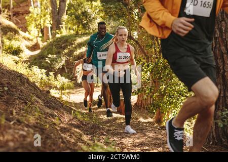 Group of athletes runners run uphill trail. Men and women running a marathon race. Stock Photo