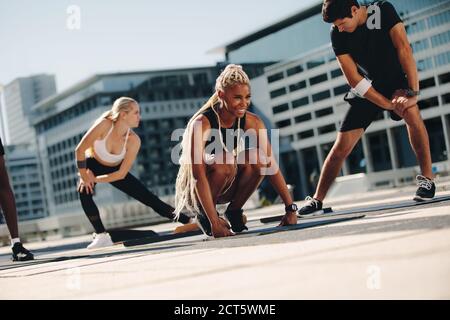 Group of people exercising together outdoors in the city. Multi-ethic men and women in sportswear doing stretching exercising.