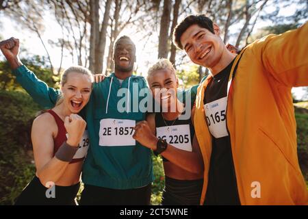 Excited group of runners celebrating their victory outdoors. Happy marathon runners after winning a race in the forest. Stock Photo