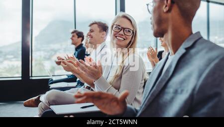 Group of businesspeople applauding speaker after conference presentation. Business men and women sitting in audience clapping hands. Stock Photo