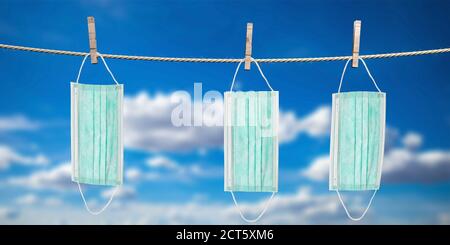 Coronavirus spread prevention measure concept. Clothespins hold three disposable surgical masks for drying on rope. Blue sky background. 3d illustrati Stock Photo