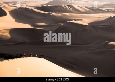 People climbing sand dunes to watch the sunset over the desert at Huacachina, Ica Region, Peru, South America Stock Photo
