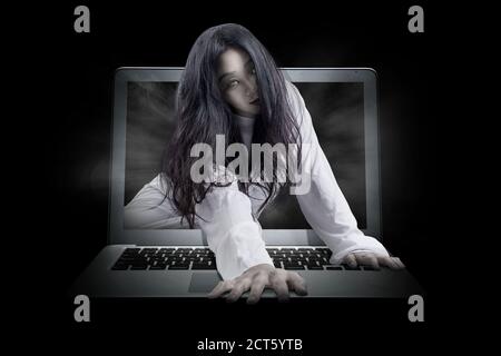 Scary ghost woman coming out from a laptop screen. Halloween concept Stock Photo