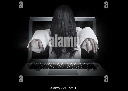 Scary ghost woman coming out from a laptop screen. Halloween concept Stock Photo