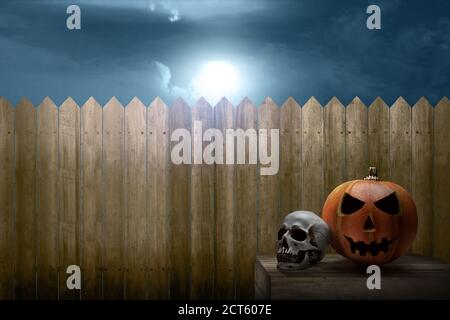 Jack-o-Lantern and human skull on the table with wooden fence and night scene background Stock Photo