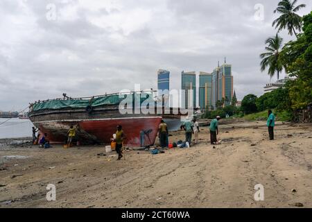 DAR ES SALAAM, TANZANIA - JANUARY 2020: Group of African Black People reparing Wooden fishing boat on the Coast of Dar Es Salaam Bay with downtown Stock Photo