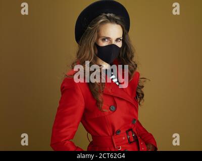 Hello autumn. modern woman in red coat with black mask isolated on beige. Stock Photo