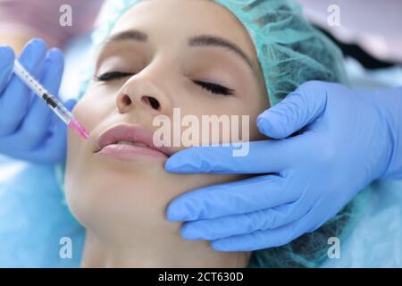 Beautician in rubber gloves makes collagen injection into lips of young woman Stock Photo